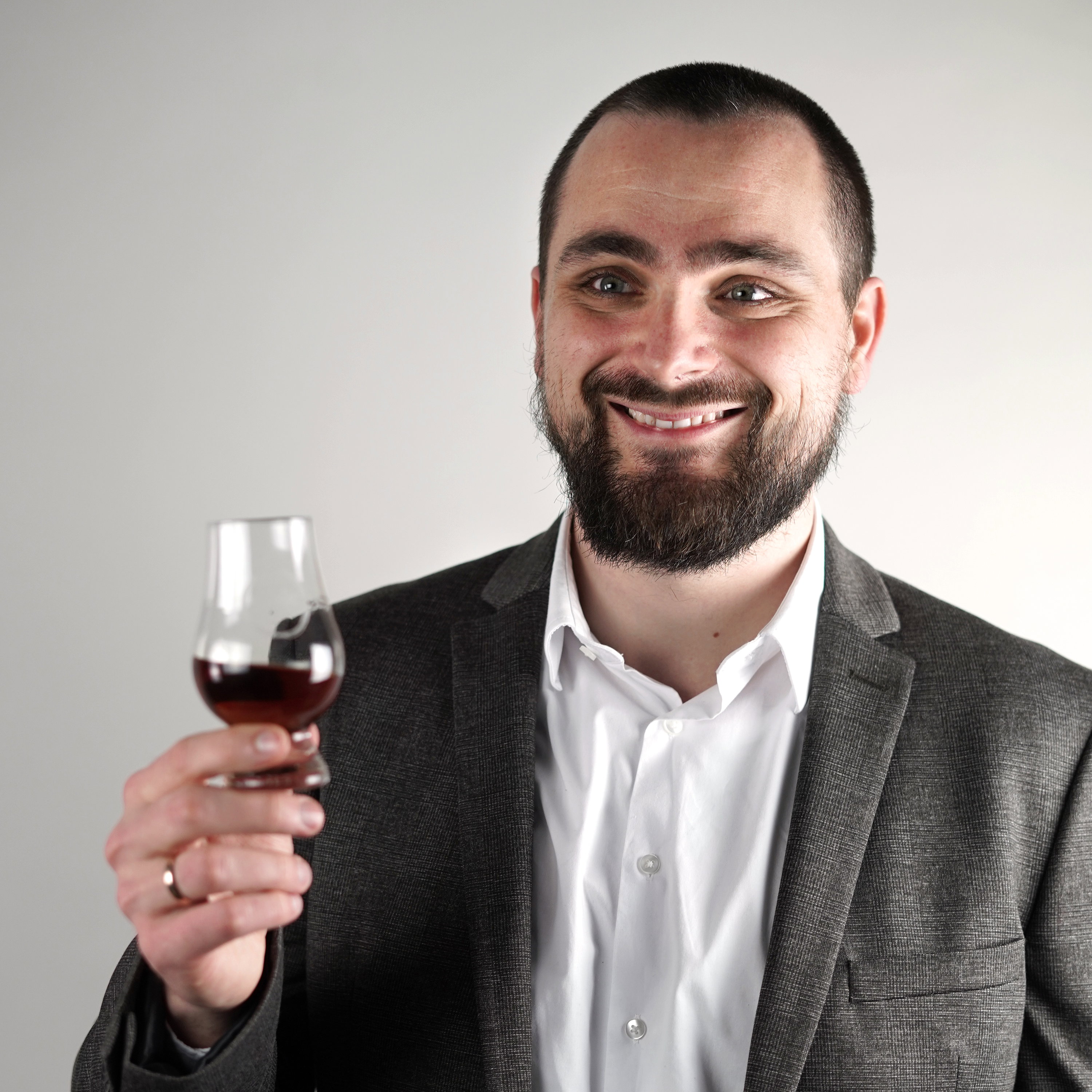 Lächelnder Genießer in Anzug hält Glas mit rotem Portwein oder Rotwein für Premium-Verkostungserlebnis