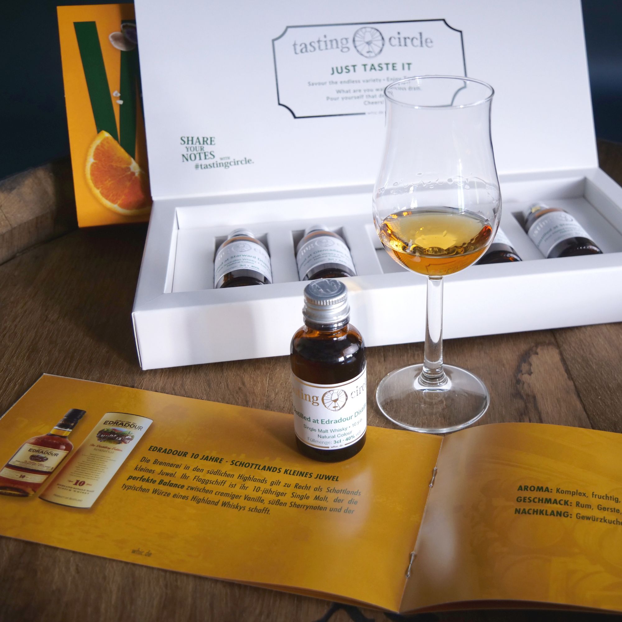 Tasting Circle Edradour 10 Jahre Single Malt Whisky Probe in offener Verkostungsbox mit 5 Miniaturflaschen und Tasting Notes Heft neben gefülltem Whiskyglas