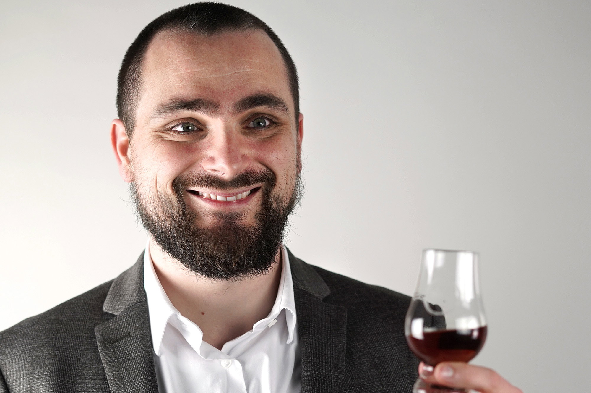 Lächelnder Genießer in Anzug hält Glas mit dunkelrotem Portwein oder Rotwein, verkostungsbereit
