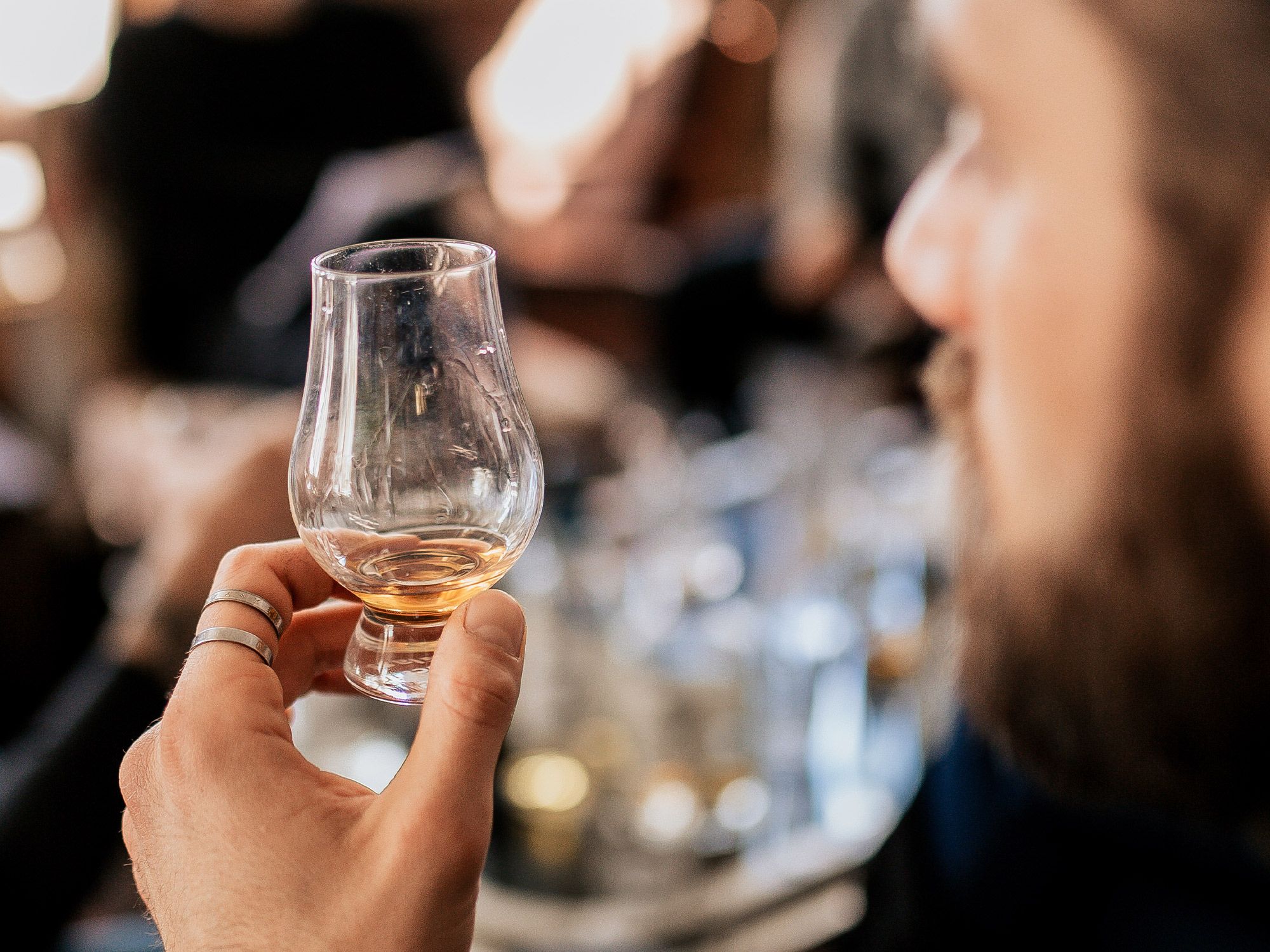 Hand hält tulpenförmiges Whisky-Glas mit bernsteinfarbenem Single Malt Whisky bei Verkostung in exklusivem Ambiente