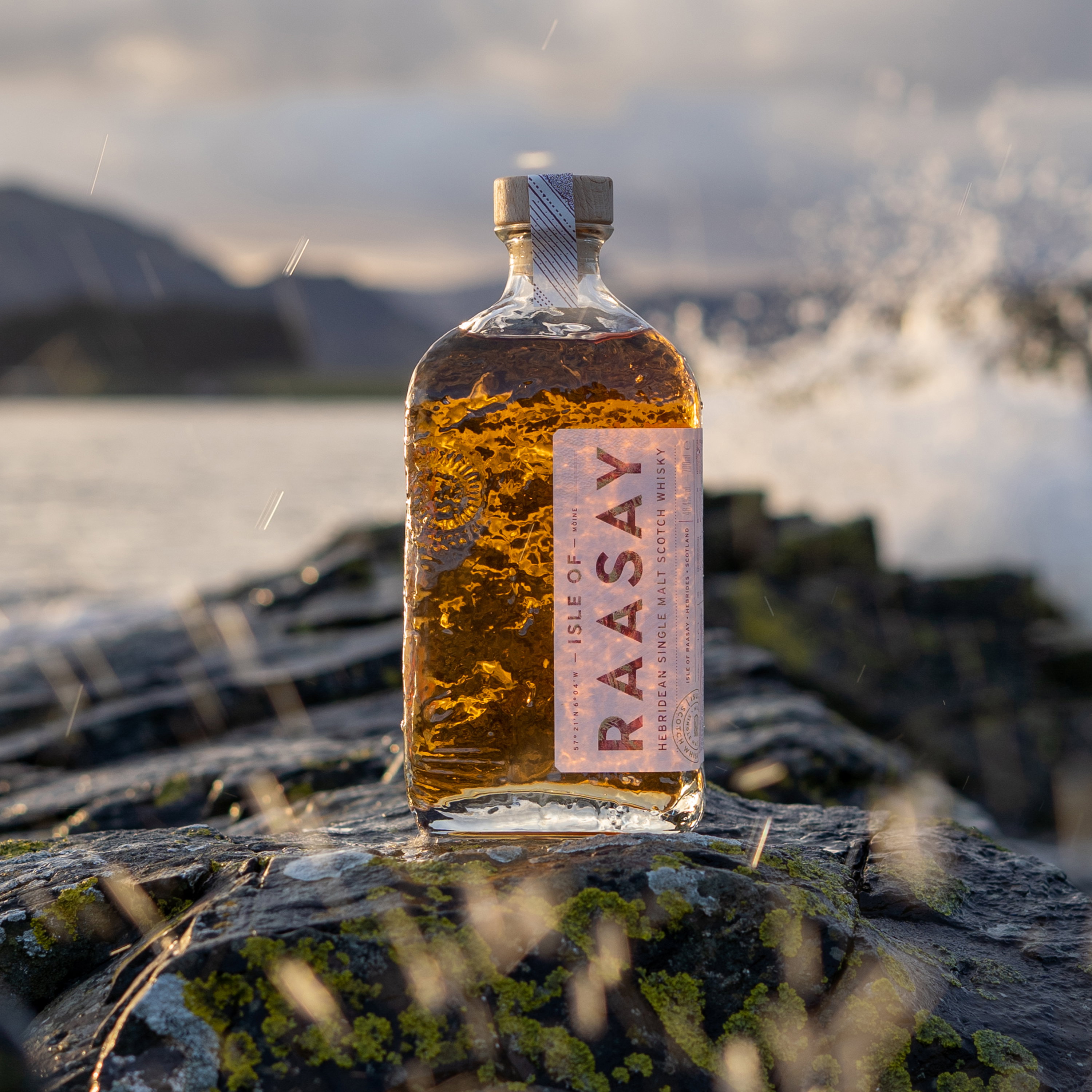 Raasay Hebridean Single Malt Scotch Whisky Flasche vor schottischer Insel-Kulisse bei Sonnenuntergang auf moosbewachsenem Felsen