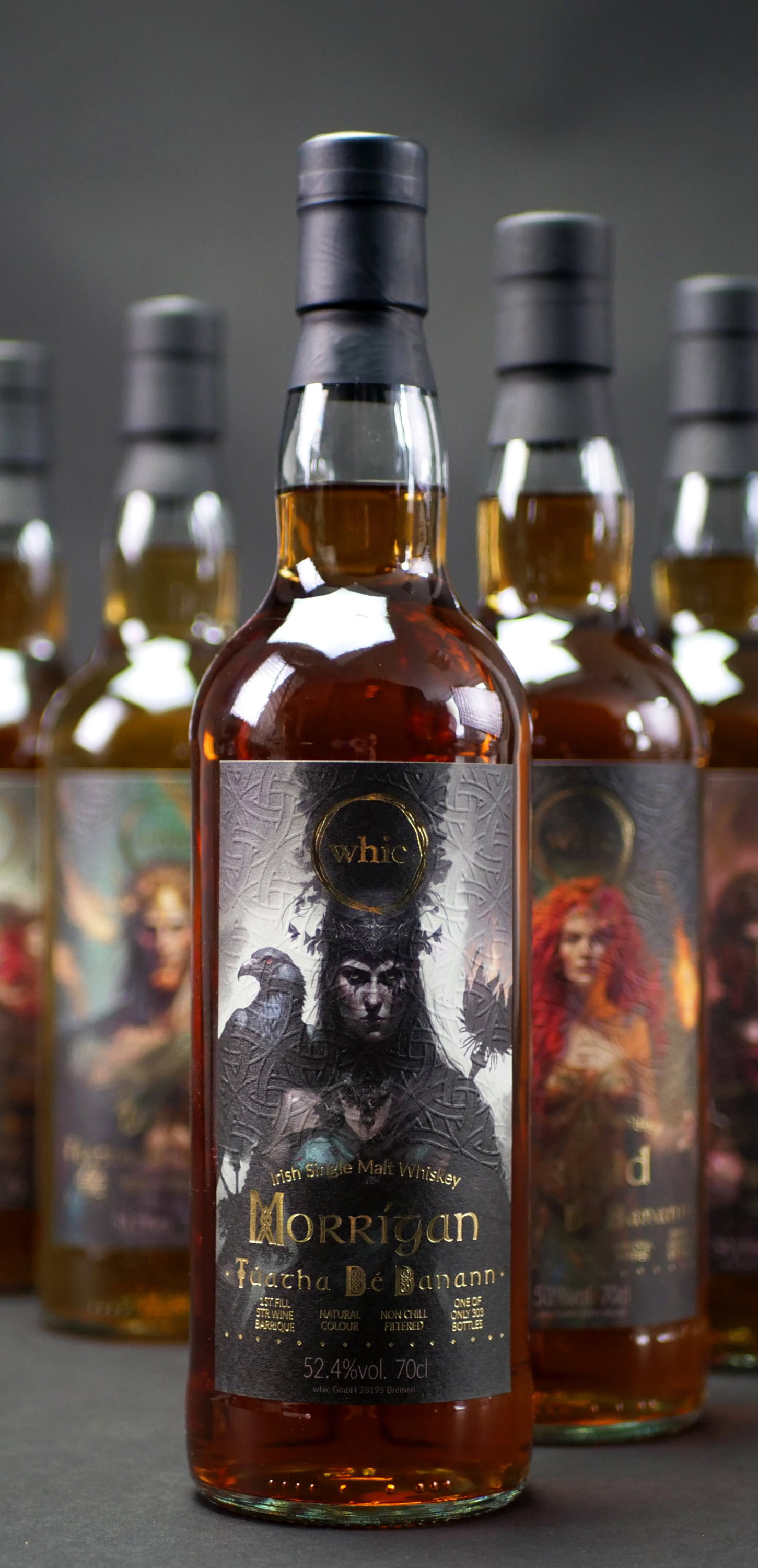 whic Morrigan Irish Single Malt Whisky Tuatha Dé Danann 52,4% vol. 0,7l mit mystischem Etikettendruck vor Gruppe gleichartiger Flaschen