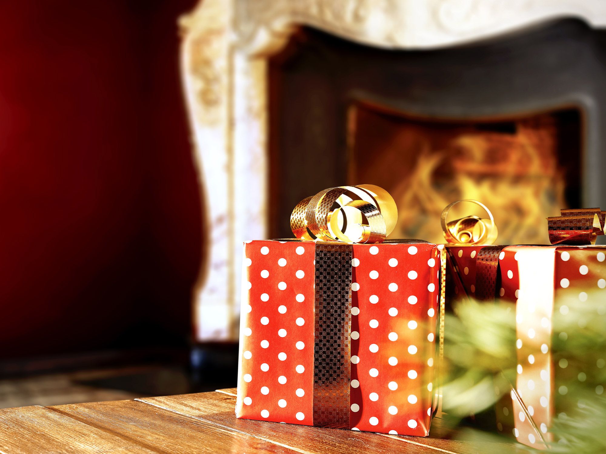 Zwei rot-weiße polka-dot Geschenkboxen mit goldener Schleife vor gemütlichem Kaminfeuer als edle Verpackungsidee für Premium-Spirituosen